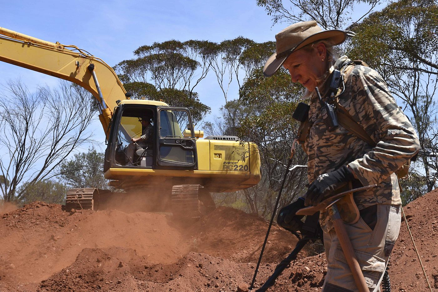Person in camo with a digger in the background
