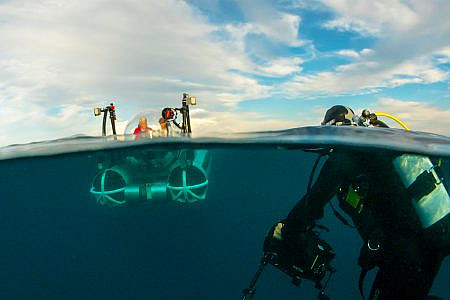 Odyssea submarine descending below the ocean surface with a camera operator in a scuba suit in the foreground