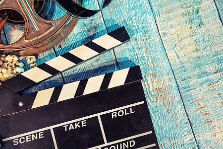 Close up of a film clapper, film reel and popcorn against a wooden background