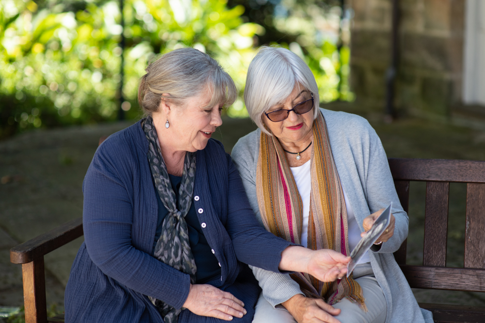 Presenter Noni Hazlehurst with participant Ellis Treleaven sitting on a bench outside looking a photo.